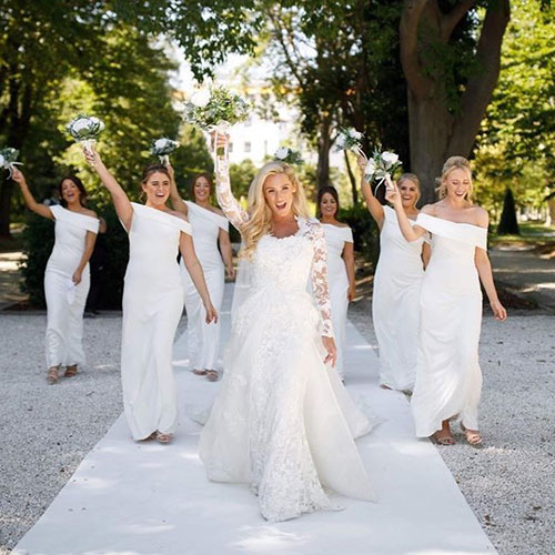 bride and six bridesmaids with white faux bouquets held up in air