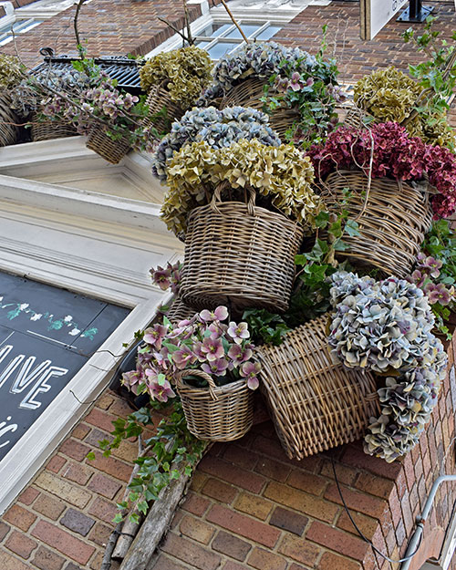 wicker baskets with pastel colour faux hydrangeas hanging on outside wall of pub over blackboard