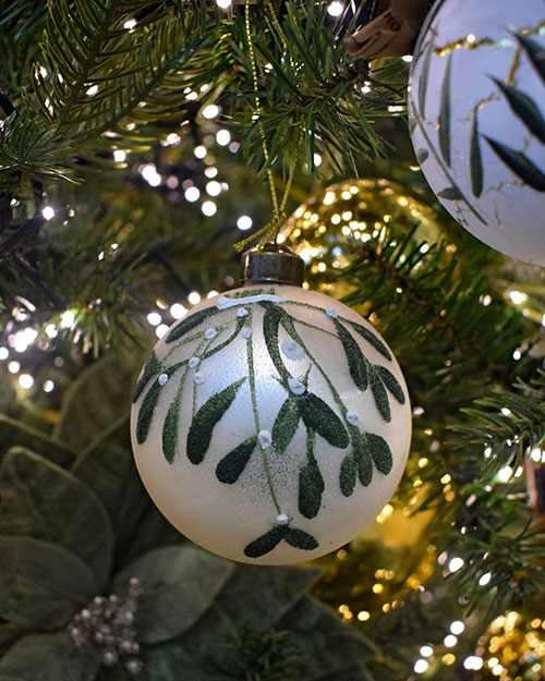 close up of gold and green christmas decorations on tree with stars, pine cones, and foliage patterns