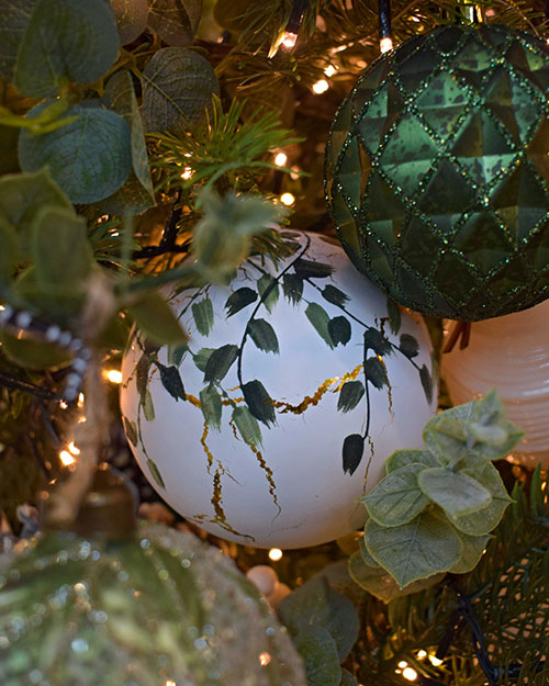 close up of green sparkly leaf pattern bauble hanging in christmas tree with white, gold and green decorations