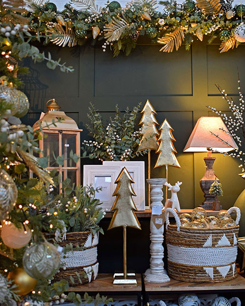 green christmas tree with white, green and gold decorations and white faux berries next to display of baskets, crates and ornaments