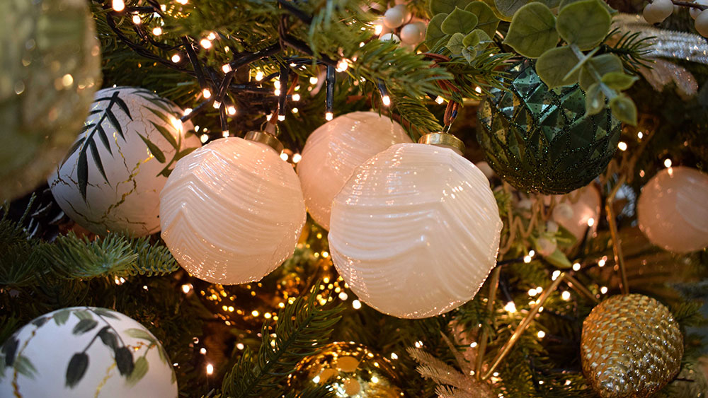 illuminated white textured baubles, green geometric baubles and gold pine cone decorations in tree