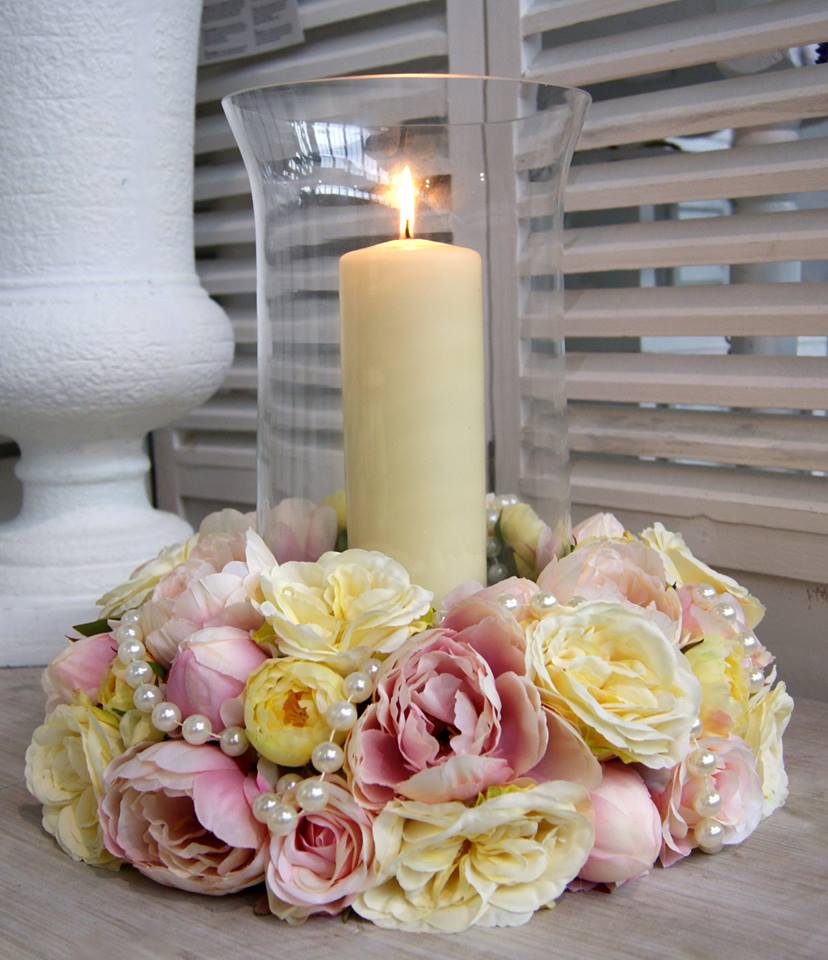 pillar church candle in vase surrounded by flowers in pink and yellow