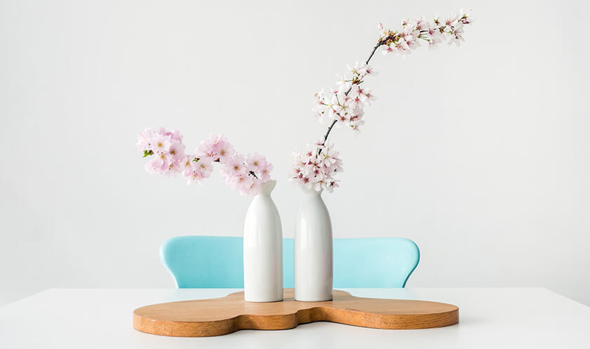 artificial blossom branches in white vases on wooden board, blue chair