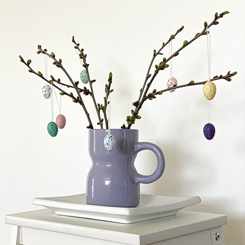 blue / purple vase with easter tree branches in bud and hanging speckled multicolour egg decorations