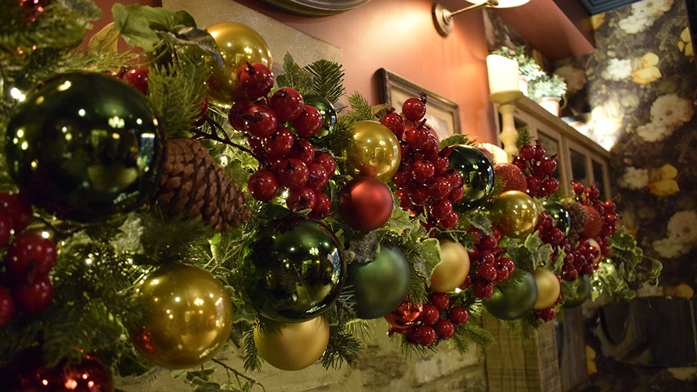 close up of artificial red berries, green and gold baubles, faux ivy Christmas garland inside pub