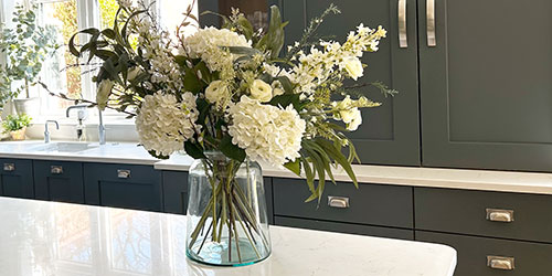 Artificial flowers bouquet of faux roses and foliage in glass vase kitchen table