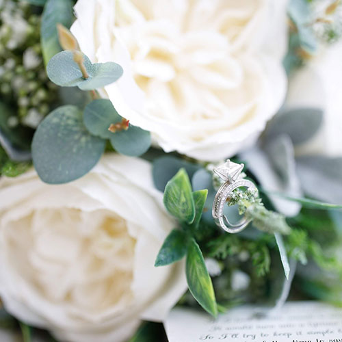 close up of white artificial rose, eucalyptus and engagement ring