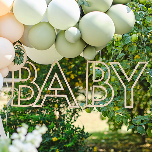 baby sign hanging from balloon arch outside near trees
