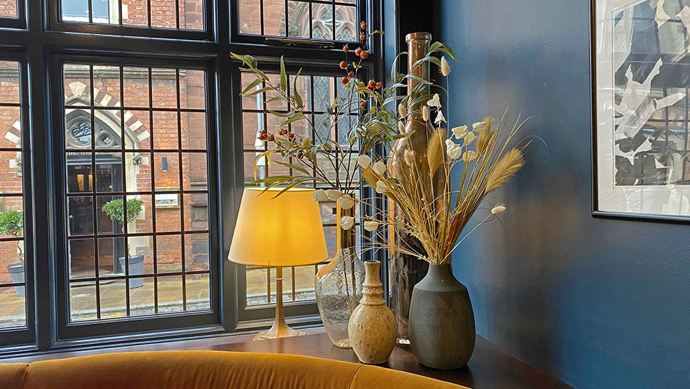 window sill in corner of bar with lamp, dried grasses, pots, vases, and artificial branches with berries