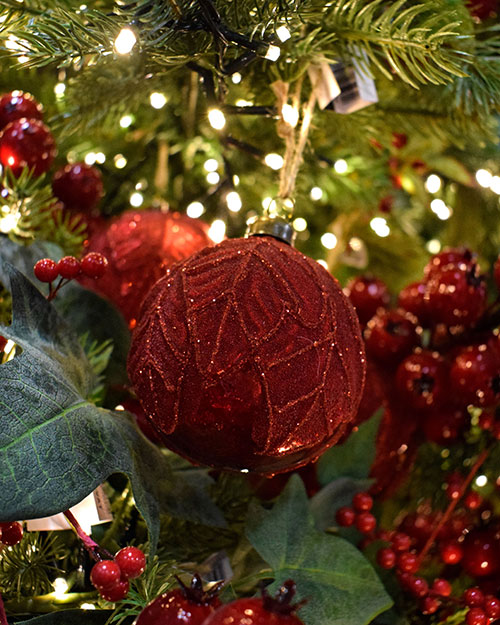 glittery dark red baubles with leaf pattern hanging in green artificial tree with faux red berries
