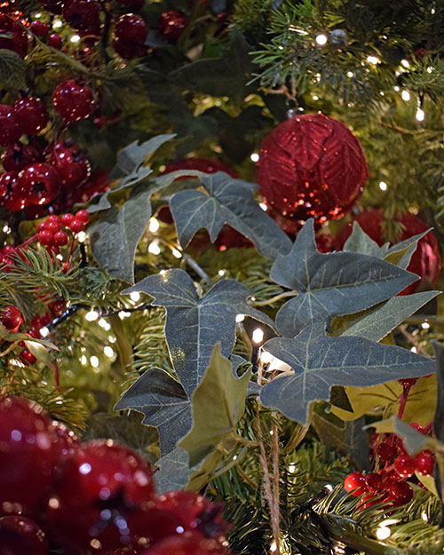 artificial ivy wound around a green Christmas tree branch with dark red berries and red wine coloured baubles