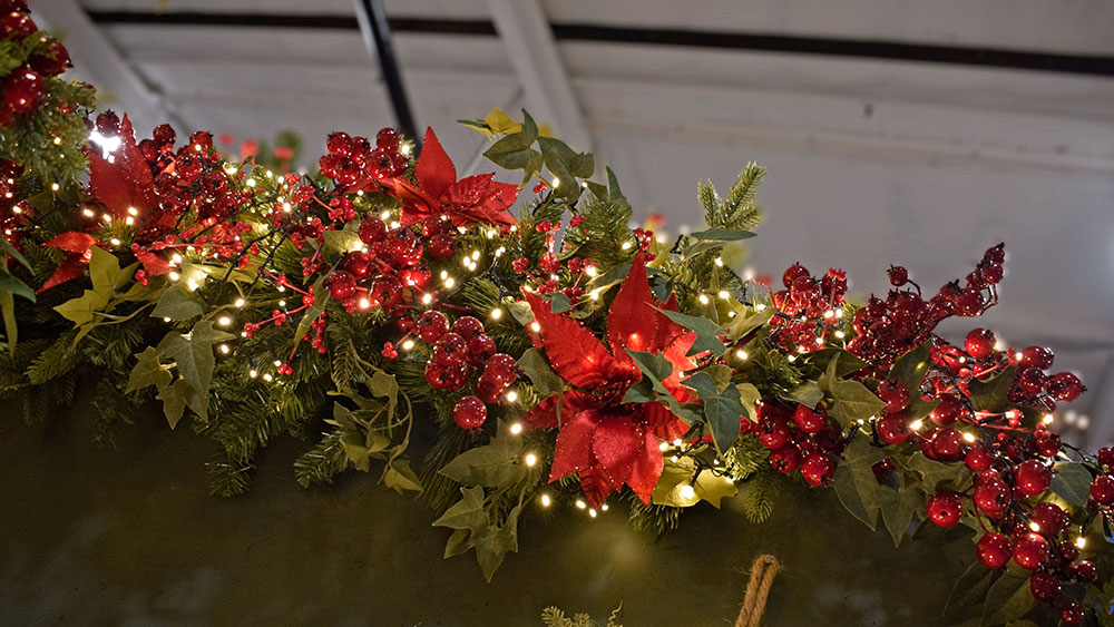 red wine themed christmas decorations on garland with faux red poinsettia, red berries, green ivy, fairy lights