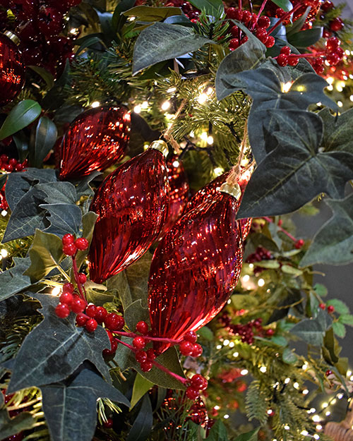 three finial drop shaped dark red baubles on Christmas tree with faux ivy, berries, and string lights