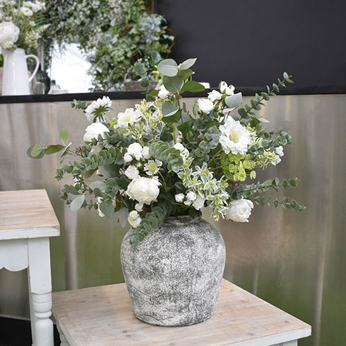delicate white and pale green bespoke artificial flowers in rustic pot on side table