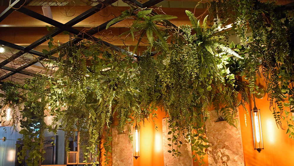 mixed faux foliage installation in a bar hanging from metal frame on ceiling