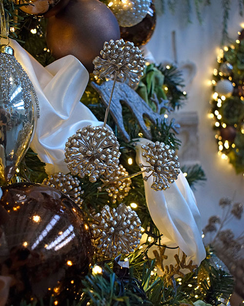 close up of champagne colour artificial allium spray in tree with cream satin ribbon, brown baubles, and lights