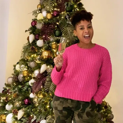 celebrity sheena lynch holding champagne glass in front of decorated christmas tree