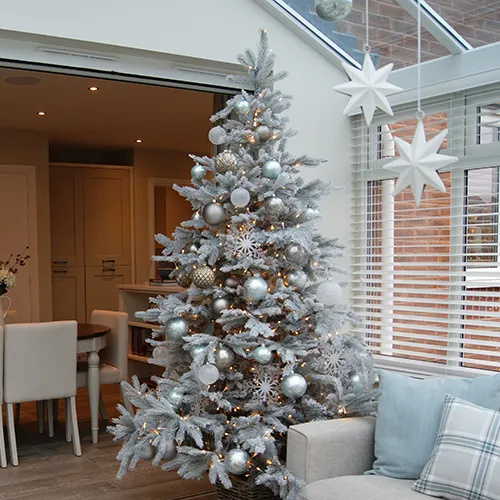 decorated white frosted christmas tree in show home with white hanging star decorations from conservatory