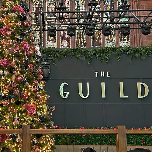 the guild in gold letters on dark panelled wall with decorated christmas tree in pink, gold, and blue