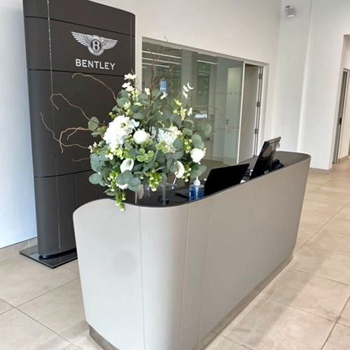 white and green bespoke corporate faux flower arrangement on reception desk at Bentley cars