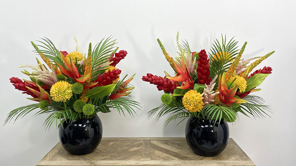 two tropical red and yellow bespoke faux flower displays in black vases on table