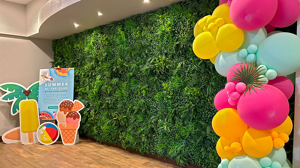 artificial plant wall for health club with summer promotional signs in front and pink, blue, and yellow balloon tower