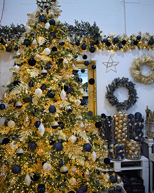 elegant blue and gold christmas tree with more decorations on display in background