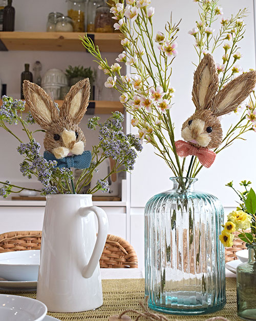 pastel easter decor straw grass bunny heads on sticks in white jug and glass vase with artificial spring flowers
