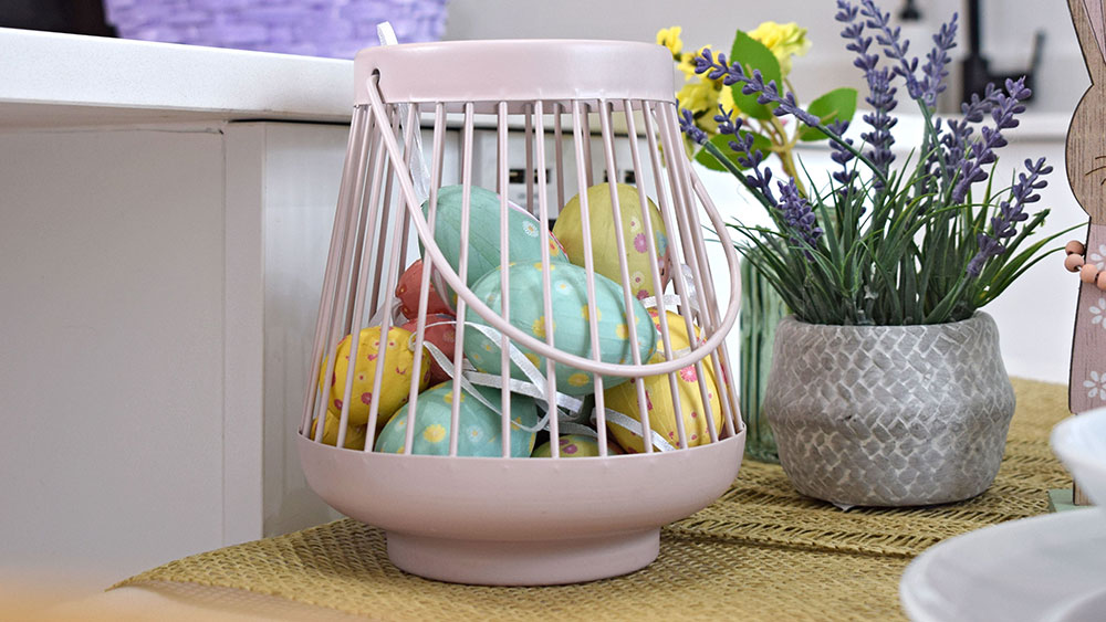 pastel easter eggs in metal basket with faux spring flowers on table