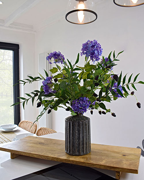 artificial purple flowers in grey vase on wooden stand