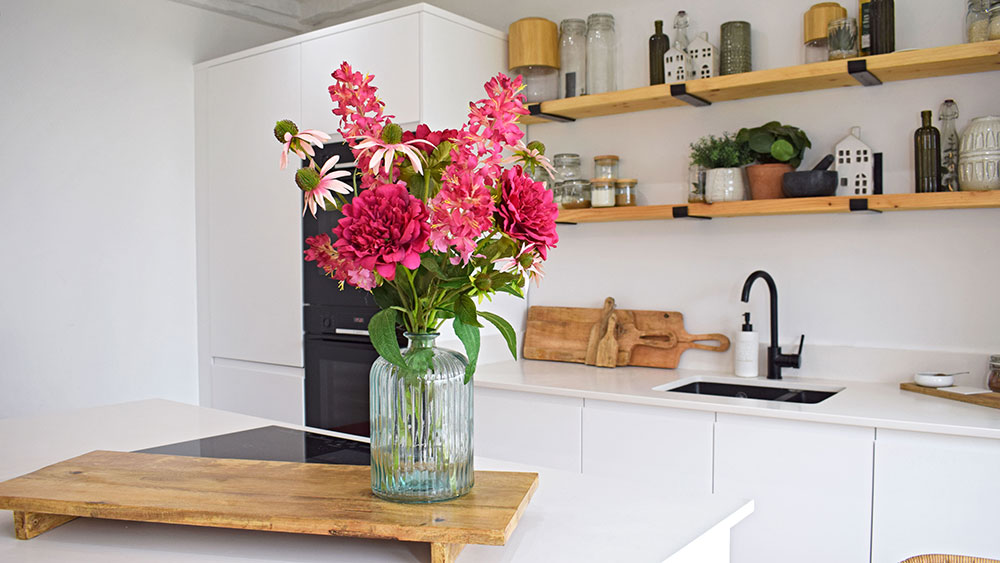 pink flower trend - collection of bright pink flowers in glass vase on wooden stand in kitchen