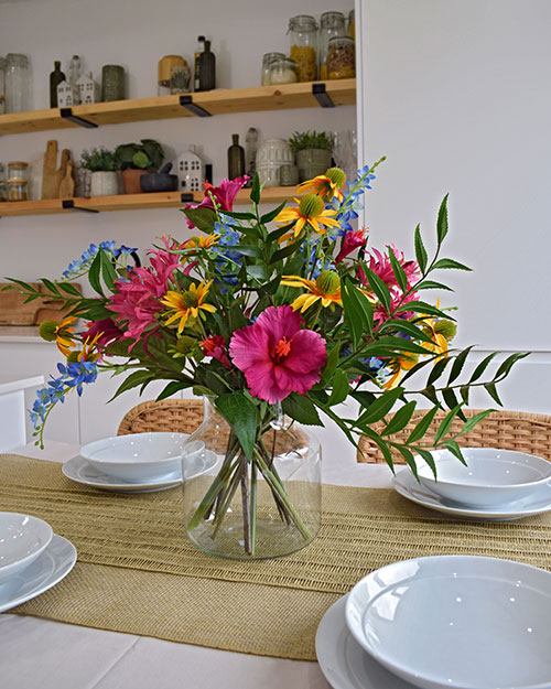 collection of viva le vida trend brightly coloured artificial flowers in glass vase on dining table