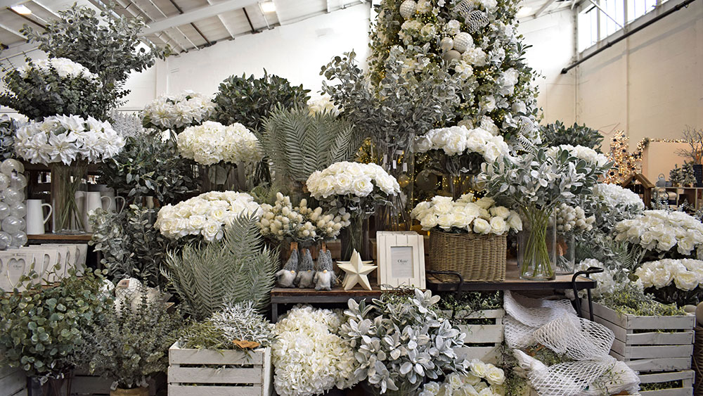 white floral and green foliage frosted christmas decorations in baskets, vases and crates