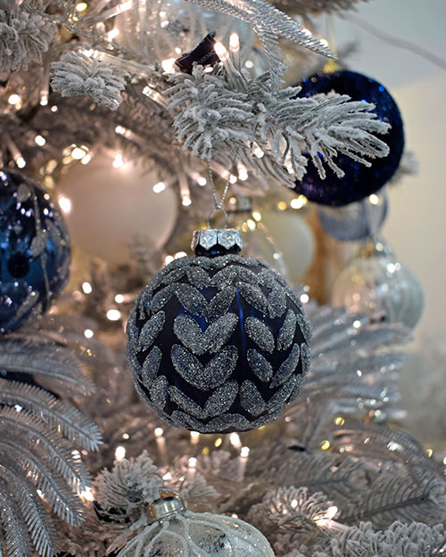 midnight blue bauble with chevron silver glitter pattern hanging from white christmas tree