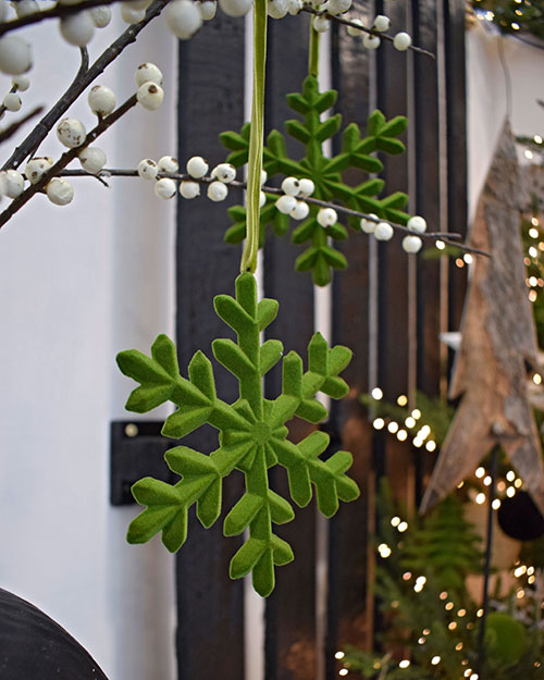 close up of green felt snowflakes hanging off artificial branch with white berries