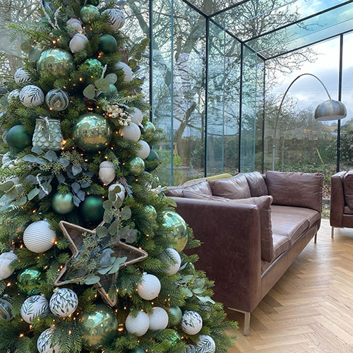 white and green xmas tree in conservatory with a brown leather sofa