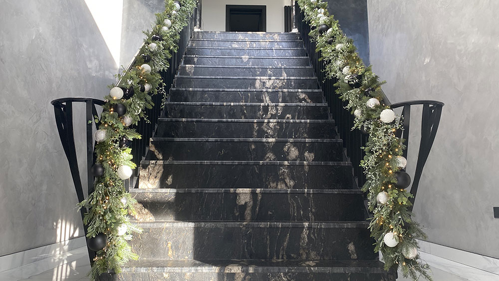 marble stairs with black banister decorated with christmas foliage and baubles in black, silver and white