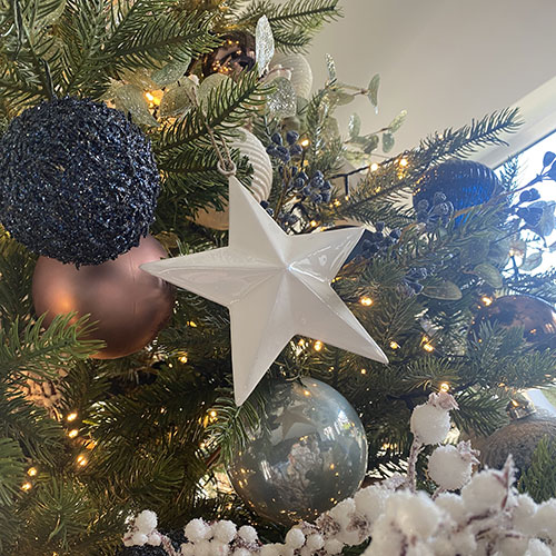 close up of christmas decorations in a tree - white star, blue, copper and silver bauble, frosted white berries