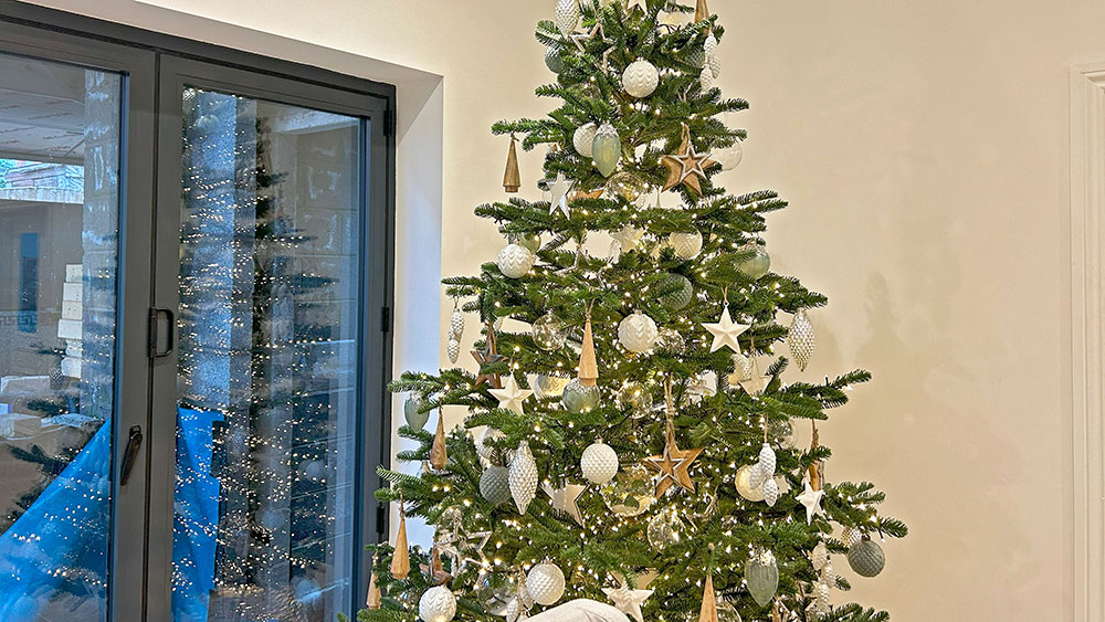 green christmas tree with silver, white, and wood decorations in a residential property with white walls and grey french doors