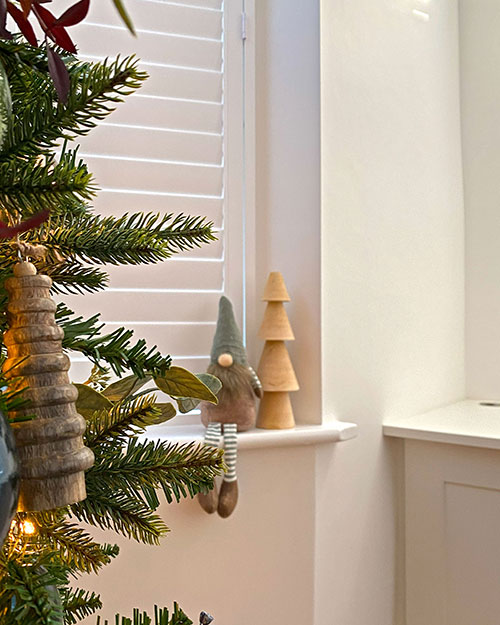 close up of wooden ribbed christmas decoration hanging from the green tree with a gonk and wooden tree ornament on the window sill