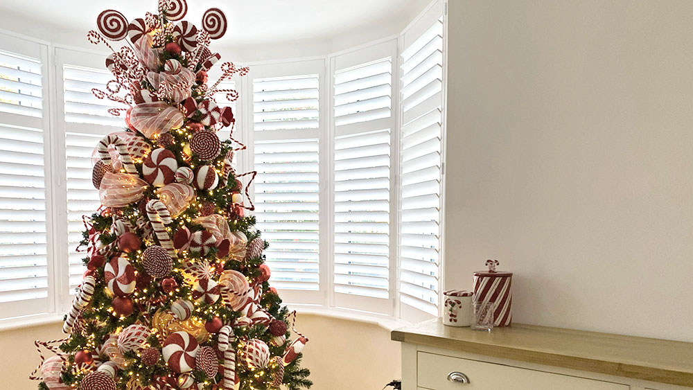 red and white candy cane themed christmas tree in white room with bay window and cupboard with candy cane jars
