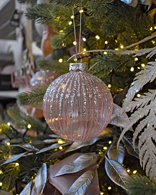 translucent baby pink bauble with silver glitter hanging on christmas tree with rose gold metallic leaves