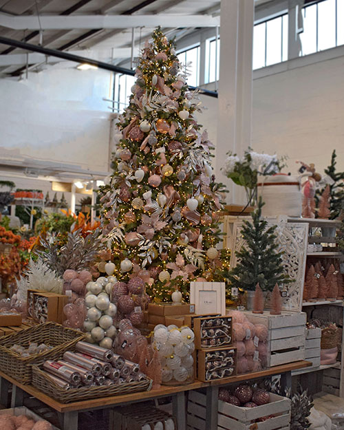 pink Christmas decorations on tall artificial tree in middle of display of more white and pink baubles in vases and baskets