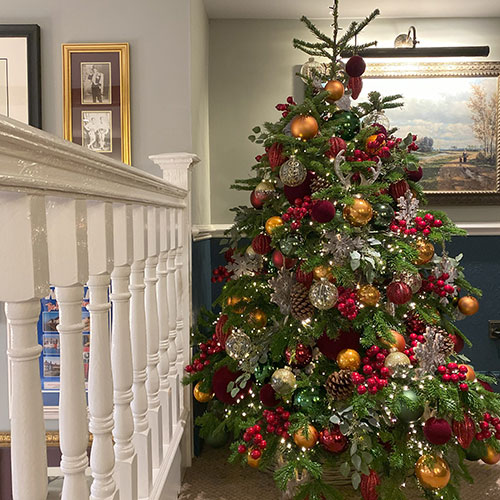 rake hall small christmas tree decorated with red, orange, berries, and snowflakes near banister