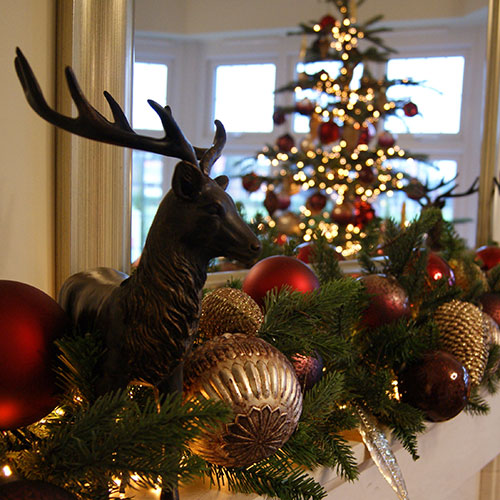stag ornament, green garland, red and gold baubles on fireplace in show home
