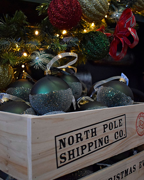 close up of wooden crate with north pole shipping co printed on it, half glitter green bauble and red ribbon