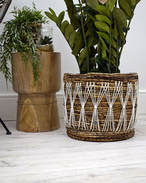 faux plant in a banana leaf planter basket with white macrame design next to wooden stool