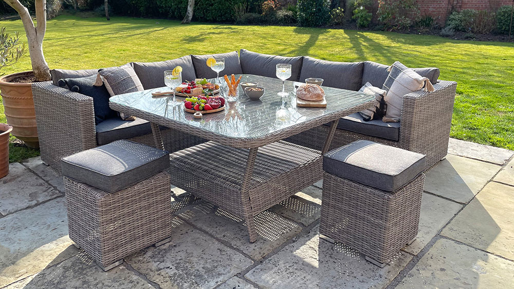 large square grey rattan outdoor dining table, corner sofa and stools with snacks and drinks