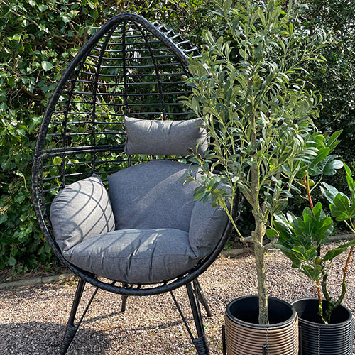black wicker standing egg chair with grey cushions on gravel in garden
